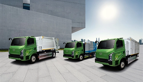 Lineup of green Daewoo Gixen eco-friendly municipal trucks including a garbage compactor, street sweeper, and refuse container truck parked on a paved plaza