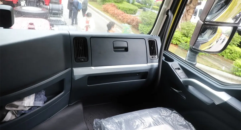 Interior passenger view of a Chenglong heavy-duty truck cab showing dashboard storage, seat and side mirror