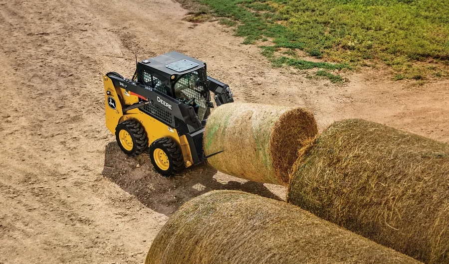 John Deere Skid Steer loader moving hay bales on a farm.